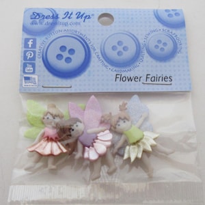 May include: A package of four flower fairy buttons. The buttons are made of plastic and have a glittery finish. The package is blue and white and says "Dress It Up" and "Flower Fairies".