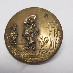 Puede incluir: Un botón de metal dorado con un diseño en relieve de dos figuras con ropa tradicional japonesa, una de ellas sosteniendo un paraguas, caminando junto a una estructura similar a una pagoda.