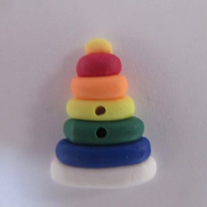 May include: A colorful stacking toy made of plastic. The toy is shaped like a pyramid and has five rings in different colors: yellow, orange, red, green, and blue. The bottom ring is white.