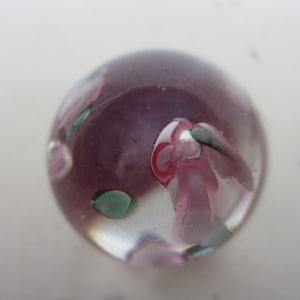 May include: A clear glass marble with pink, green, and white swirls inside.