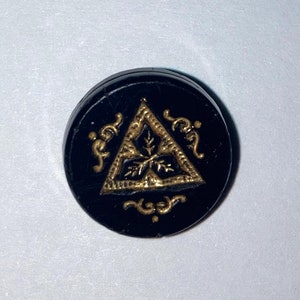 May include: Black button with a gold triangle design featuring a stylized leaf inside. The triangle is surrounded by a decorative border.