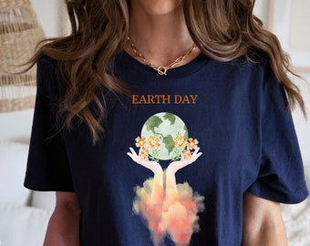 May include: Navy blue t-shirt with the text "EARTH DAY" in orange. The shirt features a watercolor design of the Earth held in two hands, surrounded by orange flowers. The design has a watercolor effect.