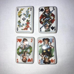 May include: Four rectangular playing card tiles. The Ace of Clubs features floral designs. The King of Spades is depicted with a crown and scepter. The Queen of Hearts and Jack of Diamonds are also shown. Each tile has a white background.