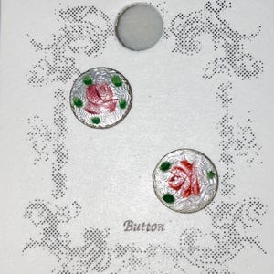May include: A set of three buttons on a white card. Two round buttons feature a red rose design with green accents and a silver border. The word "Button" is printed in the center.