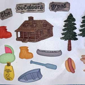 May include: A collection of decorative charms featuring a brown log cabin, two green pine trees, a red boot, a yellow boot, a grey canoe, a blue paddle, a hot dog, a moose, a watermelon slice, a bottle of dark tanning oil, and signs reading the outdoors great.