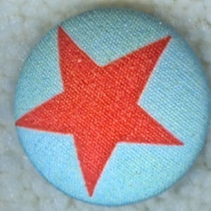 May include: A red star on a light blue background. The star is a simple five-pointed star with a slightly textured surface. The background is a smooth, light blue fabric.