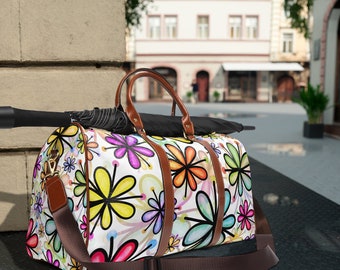 May include: A white travel bag with a brown leather trim and a colorful floral pattern. The bag has a large main compartment and a smaller front pocket. The bag is sitting on a black surface.