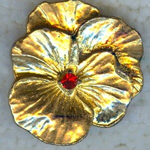 May include: A gold-colored metal flower pin with a red gemstone center. The pin has three petals and is designed to resemble a pansy. The metal has a slightly aged appearance.