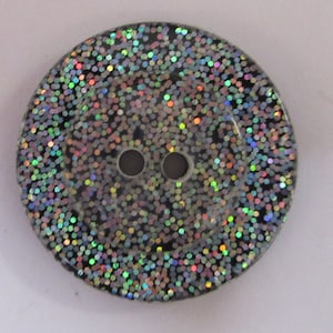 May include: A black button with iridescent glitter covering the surface. The button has two holes.
