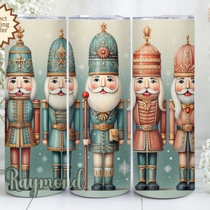 Puede incluir: Un juego de cinco vasos con un diseño repetido de soldados cascanueces en verde azulado, rojo y dorado. Los vasos tienen un fondo verde claro con copos de nieve y el nombre "Raymond" en la parte inferior. Las palabras "Perfect Stocking Stuffer" están en una estrella.