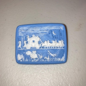 May include: A rectangular, light blue ceramic plaque with a white bas-relief scene of a horse-drawn carriage, figures, and a crescent moon. The plaque has rounded corners and a smooth surface.