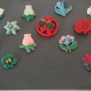 May include: Assortment of vintage plastic flower brooches in various colors, including blue, pink, red, green, and white. The brooches feature different flower designs, such as roses, tulips, and daisies.