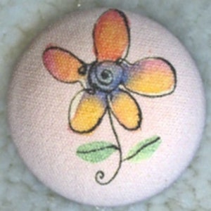 May include: A pink fabric button with a hand-painted orange, yellow, and blue flower design.