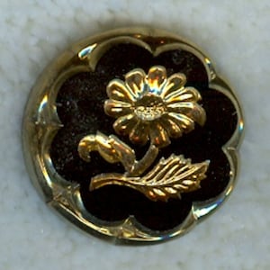 May include: A gold-colored flower with a black background. The flower has a detailed design and is set in a decorative frame.