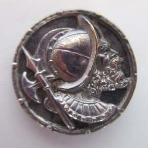 May include: Silver-toned metal button featuring a detailed relief design of a warrior wearing a helmet and holding a spear. The warrior's face is visible and has a beard.