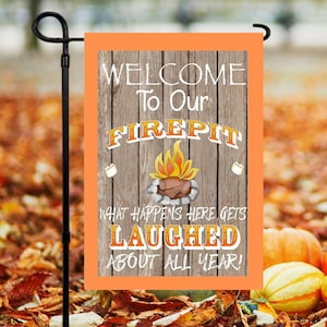 Puede incluir: Una bandera de jardín con un borde naranja y un fondo de madera. La bandera dice "WELCOME To Our FIREPIT" con un gráfico de una fogata y malvaviscos. También se muestra el texto "WHAT HAPPENS HERE GETS LAUGHED ABOUT ALL YEAR!"