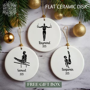 May include: White ceramic disk ornaments with gymnast illustrations in black. Each ornament has a gold string for hanging and features a gymnast's name and the year 2025. The text "FLAT CERAMIC DISK" is at the top.