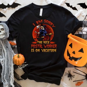 May include: Black t-shirt with a Halloween-themed graphic. The design features a witch on a broom in front of a red moon, with the text "I AM SORRY THE NICE POSTAL WORKER IS ON VACATION."