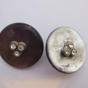 May include: Two round buttons with a silver finish and three clear rhinestones in a triangular pattern.