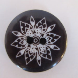 May include: A black button with a white mandala design. The button has two holes.