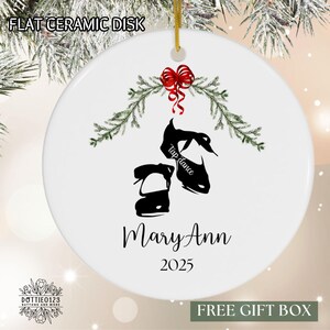 May include: White ceramic disk Christmas ornament with a gold string. The ornament features a black silhouette of tap shoes, the words "Tap dance", the name "Mary Ann", and the year "2025". A red bow and green sprigs decorate the top.