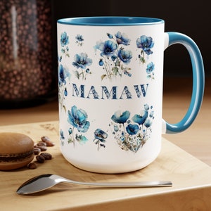 May include: White ceramic mug with a blue rim and handle. The mug features a floral design with blue poppies and the word "MAMAW" in blue lettering.