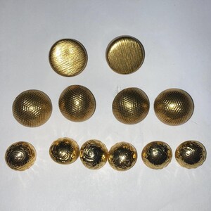 May include: A collection of gold-colored buttons in various sizes and textures. The buttons include smooth, ridged, and patterned designs. These buttons are likely for sewing or crafting projects.