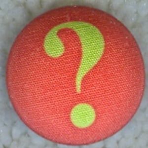 May include: A red fabric button with a bright green question mark in the center.