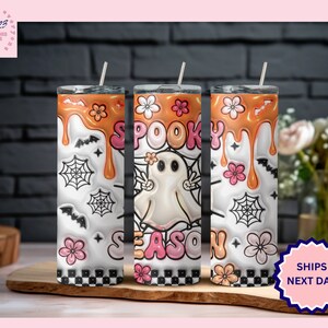 May include: Three stainless steel tumblers with a white background and orange, pink, and black designs. The tumblers feature a ghost, spiderwebs, and the text "Spooky Season".