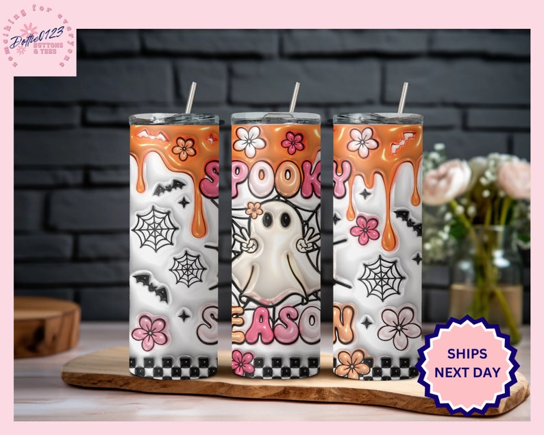 May include: Three stainless steel tumblers with a white background and orange, pink, and black designs. The tumblers feature a ghost, spiderwebs, and the text "Spooky Season".