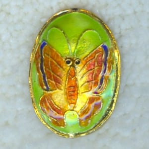 May include: Oval-shaped, gold-toned pendant with a green enamel background and a colorful butterfly design. The butterfly has orange, red, and yellow wings with blue accents.