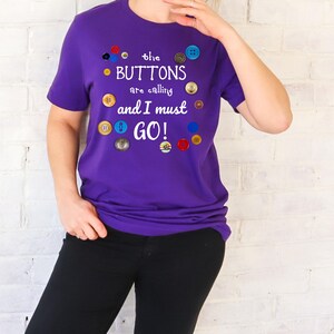 May include: Purple t-shirt with the text "the BUTTONS are calling and I must GO!" surrounded by colorful buttons.