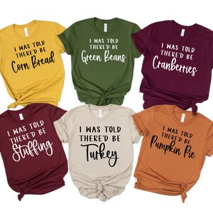 May include: A collection of six short-sleeved t-shirts in various colors, each with the phrase "I WAS TOLD THERE'D BE" followed by a different Thanksgiving food item in a script font. The colors include gold, green, burgundy, beige, orange, and maroon.