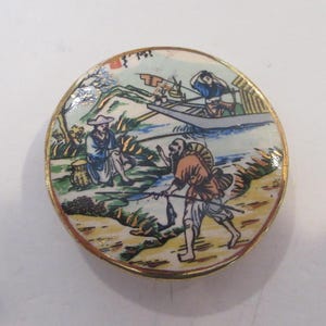 May include: A round ceramic tile with a gold rim depicting a scene of three men fishing in a river. The tile has a white background with a blue river, green grass, and brown mountains. The men are wearing traditional Japanese clothing and are holding fishing poles. One man is in a boat, while the other two are standing on the riverbank.
