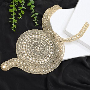 May include: A gold-toned embroidered neckline applique featuring a circular medallion design with small reflective mirror accents and delicate beadwork on a sheer mesh base, extending into a curved collar shape with matching metallic embroidery.