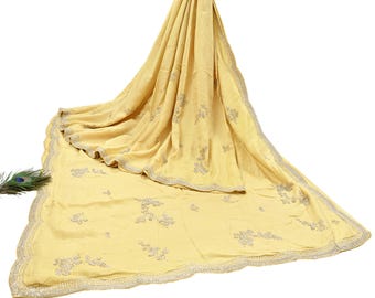 May include: A pale yellow saree with intricate silver embroidery. The fabric drapes elegantly, showcasing floral and leaf patterns along the border and scattered across the surface. A peacock feather adds a decorative touch.