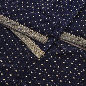May include: Navy blue fabric with a repeating pattern of small, gold-colored squares. The edges are trimmed with a detailed gold embroidered border. The fabric is folded, showing the texture and design.