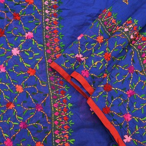 May include: A vibrant blue fabric featuring intricate embroidery with yellow vines and small flowers in shades of red, pink, and orange. The textile includes a distinct vertical border pattern and a solid red hem along the folded edge of the material.