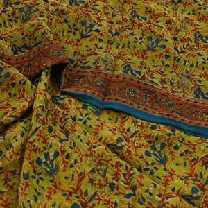Pode incluir: Um tecido verde com um padrão floral em tons de azul, vermelho e amarelo. O tecido tem uma borda com um padrão repetitivo.