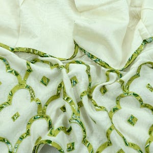 May include: White fabric with a green geometric pattern. The fabric is folded and has a soft, textured look.