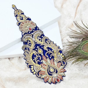 May include: An elaborate blue embroidered applique with gold, red, and yellow detailing. The design incorporates floral and paisley motifs, adorned with rhinestones. This applique is likely intended for decorating garments or accessories.