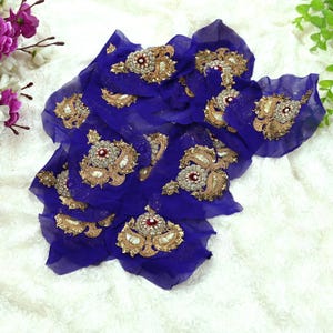 May include: Royal blue fabric with ornate gold and silver embroidery. The fabric is adorned with multiple decorative elements featuring red and clear gemstones. The design is likely for embellishment or decorative purposes.