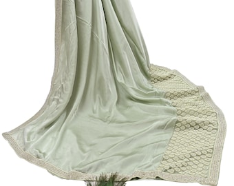 May include: A draped, pale green velvet shawl with a decorative border. The border features a repeating pattern of small, embroidered circles. The edges are trimmed with a thin, metallic gold thread. A peacock feather is at the bottom.