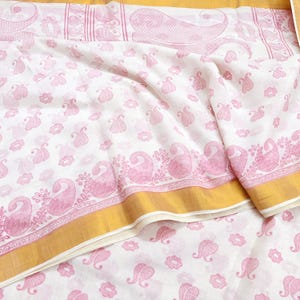 May include: White fabric with a pink paisley pattern and a gold border. The fabric has a repeating pattern of small paisley shapes and larger paisley designs along the edges. The gold border adds a touch of elegance to the textile.