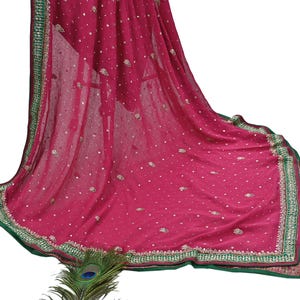 May include: A flowing magenta fabric with a green and gold embroidered border. The fabric is adorned with small, scattered embellishments. A peacock feather is visible at the bottom of the image.