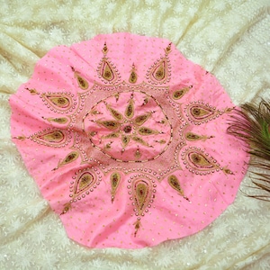 Puede incluir: Una tela circular rosa con intrincados bordados de oro y perlas. El diseño presenta un estallido de estrella central rodeado de motivos en forma de lágrima.