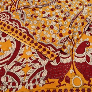 May include: A close-up of a yellow textile with a detailed pattern. The design features red and white floral and bird motifs. The fabric has a decorative border with small red flowers.