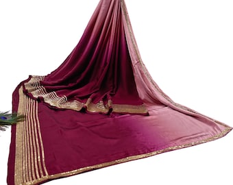 May include: A draped, two-toned saree in shades of burgundy and blush pink. The fabric features gold trim along the edges and a decorative border. The saree is made of a soft, flowing material.