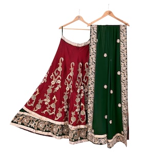 May include: A formal, two-piece outfit, including a burgundy skirt and a green shawl, both with intricate gold embroidery. The skirt is full-length, and the shawl is draped over a wooden hanger. The outfit is designed for special occasions.