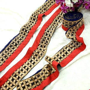 May include: Decorative trim featuring a black floral pattern with gold accents on a red and blue background. The trim is arranged in a flowing pattern, with a rolled-up section visible. The trim is suitable for various craft and sewing projects.